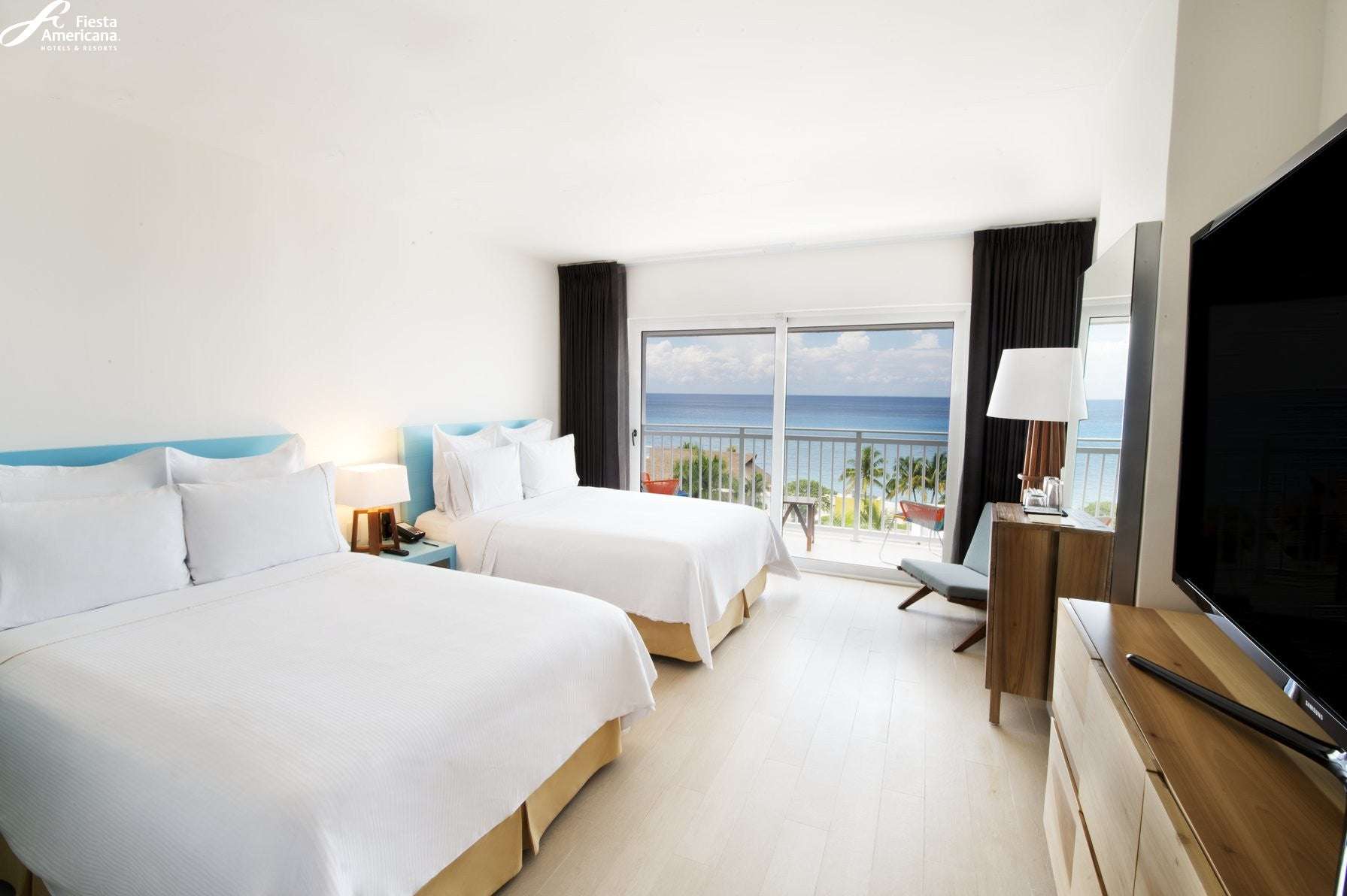 Modern hotel room with two beds, a TV, and a view of the ocean.